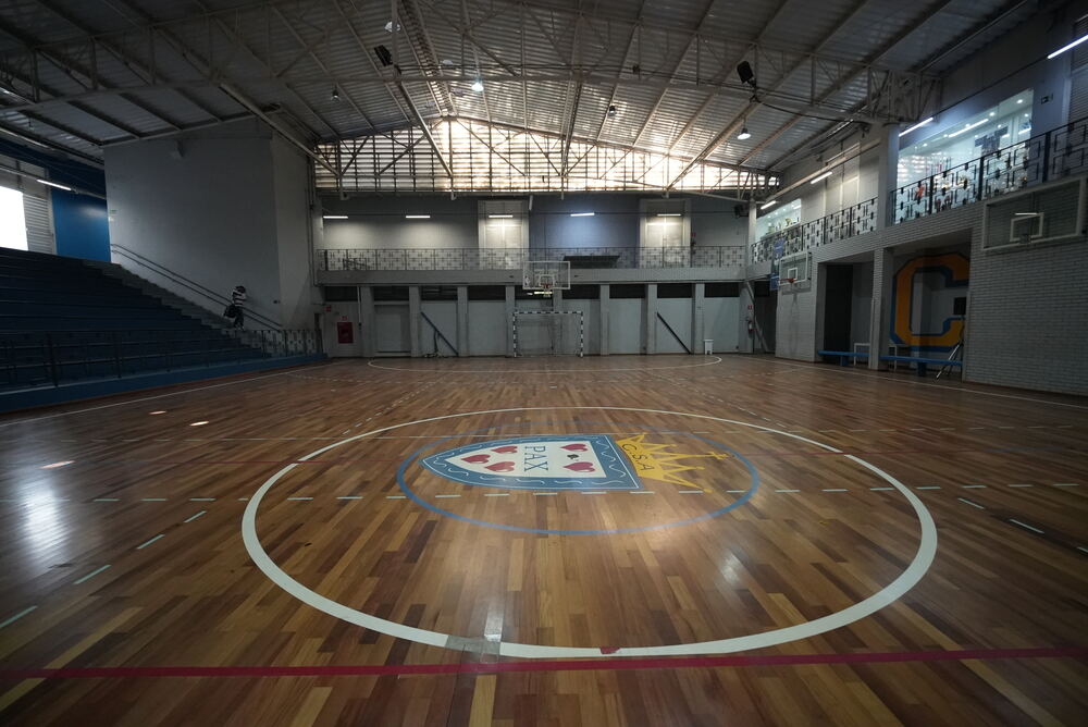 Quadra poliesportiva com piso de madeira restaurado e brasão do clube